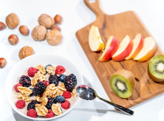 A nutritious breakfast bowl featuring fresh berries and walnuts, served with sliced fruit and kiwi.