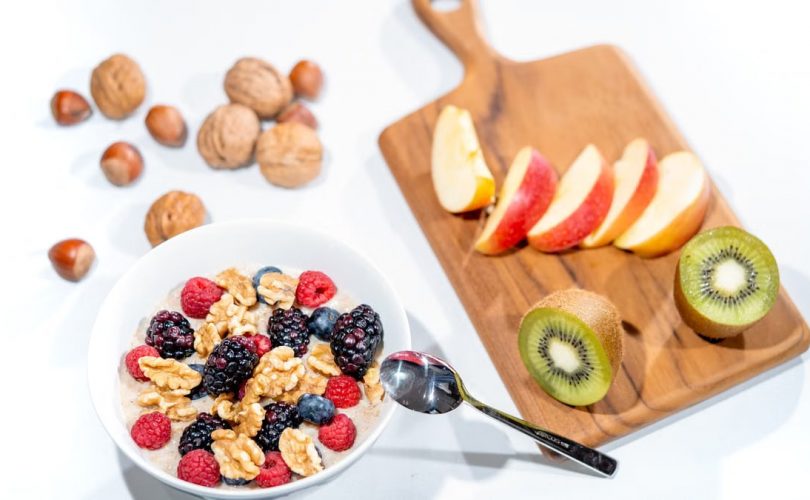 A nutritious breakfast bowl featuring fresh berries and walnuts, served with sliced fruit and kiwi.