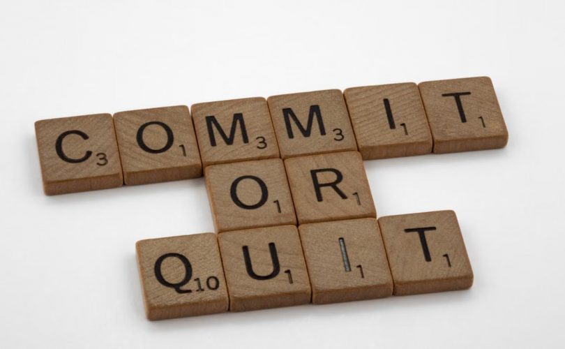 Wooden Scrabble tiles arranged to form the words 'Commit or Quit' on a white background.